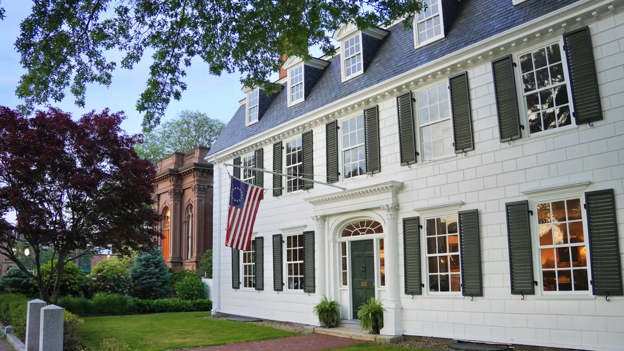 White colonial house with dark shutters behind a lawn
