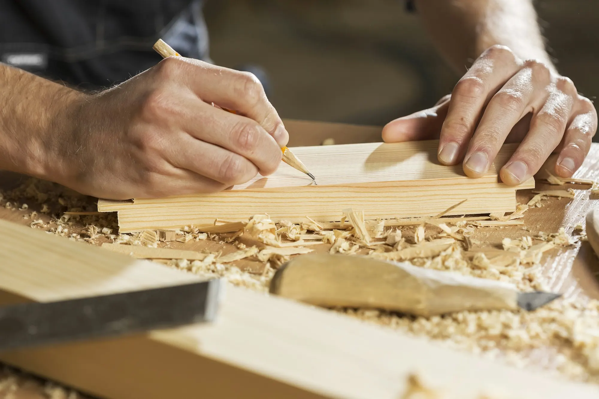 Carpenter hand-planing a board, with wood shavings on the bench